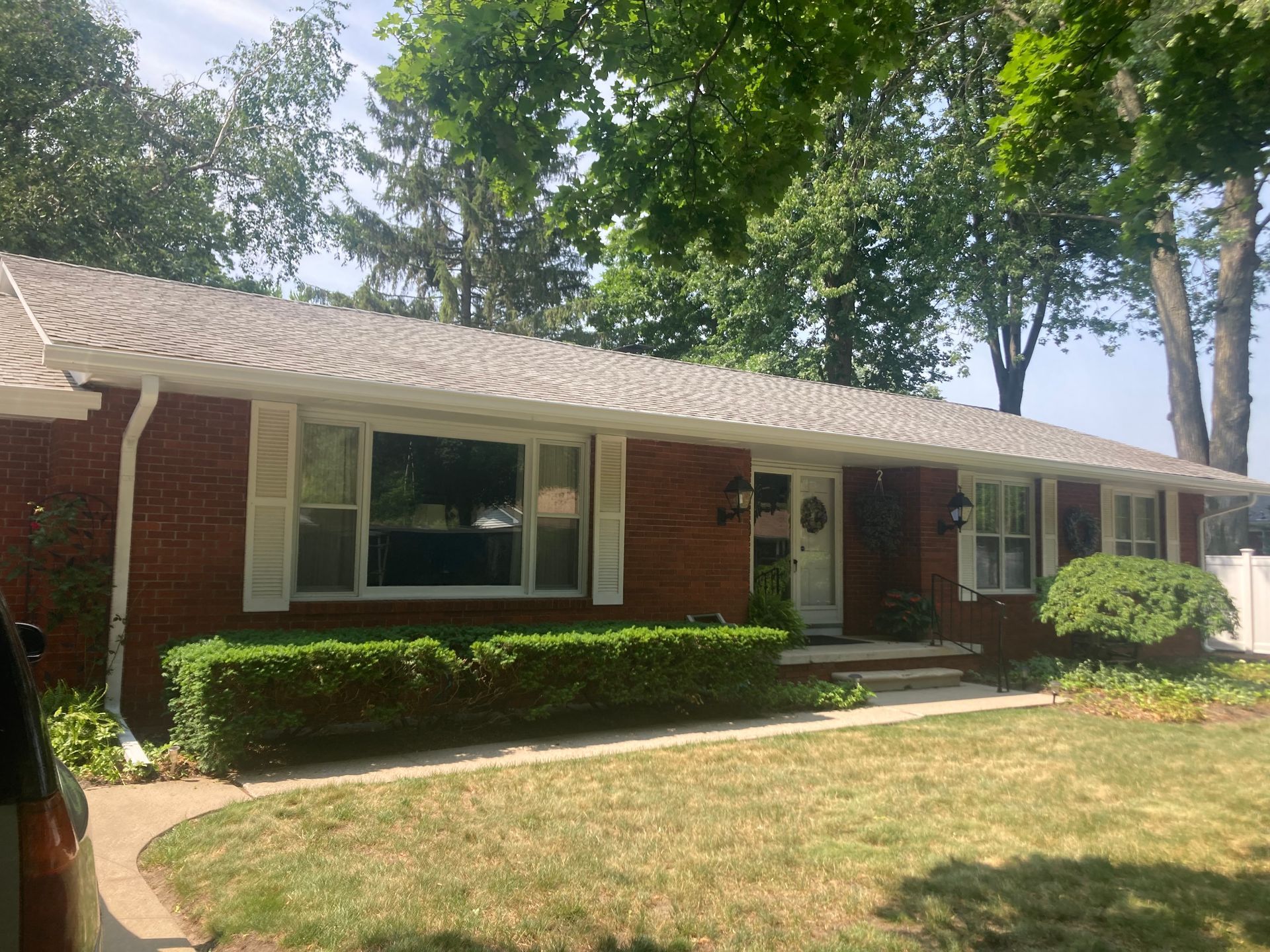 Red brick house with white shutters, green lawn and shrubs, and trees.