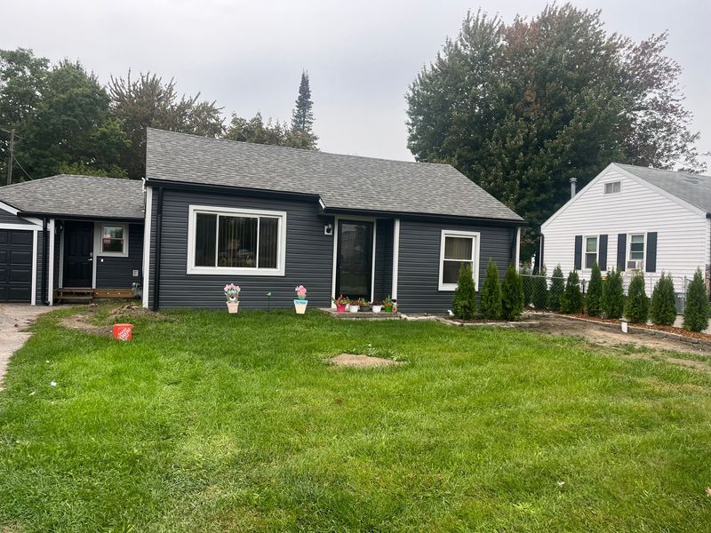 Dark gray house with white trim and gray roof; small lawn with potted plants and trees.