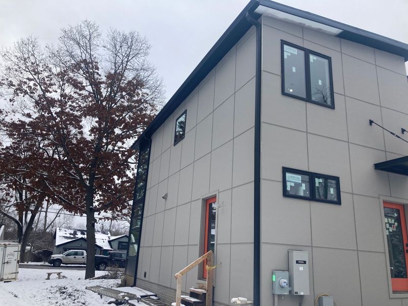 Modern two-story building with gray panels, black trim, and orange door frames in a snowy outdoor setting.