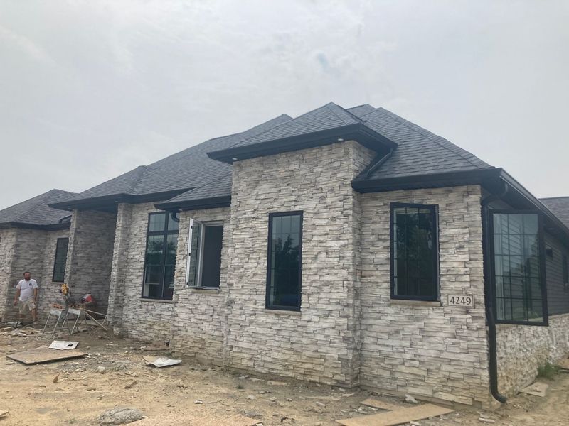Gray stone veneer house under construction with black framed windows and a dark roof.