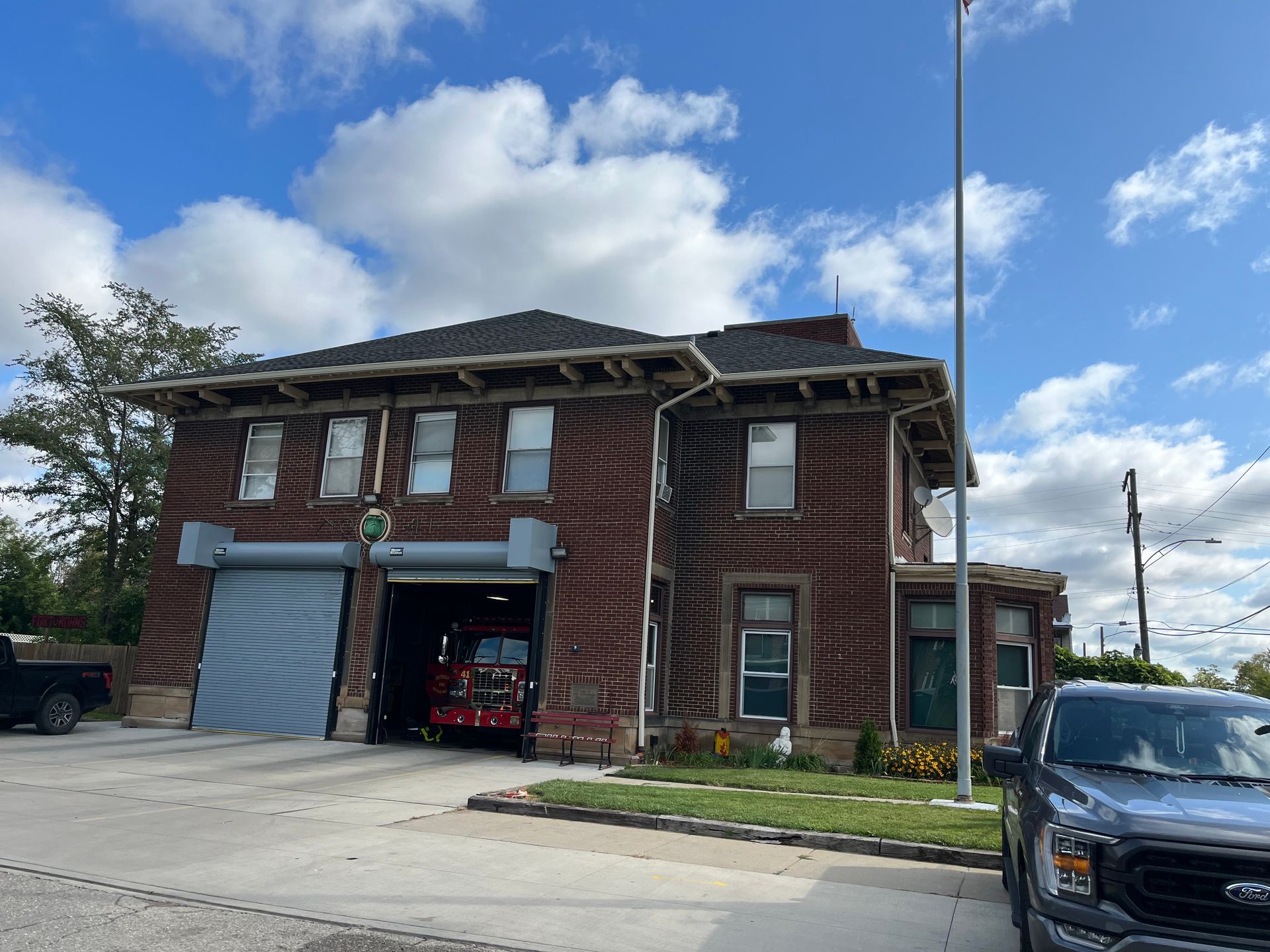 Brick fire station with open garage doors and fire truck visible, blue sky.