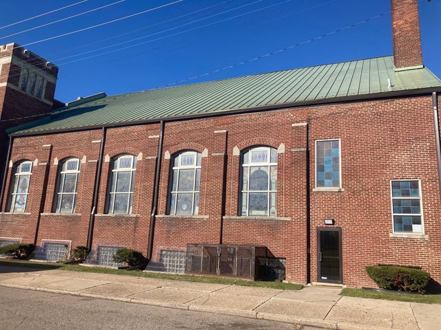 Red brick church building with arched windows, green roof, and a clear blue sky.