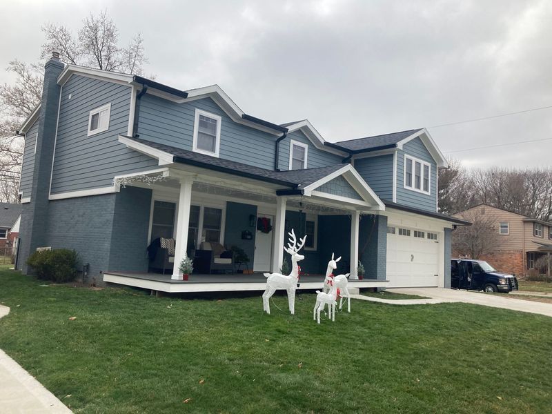 Blue house with white trim, porch, and garage. Lawn decorated with white reindeer. Cloudy sky.
