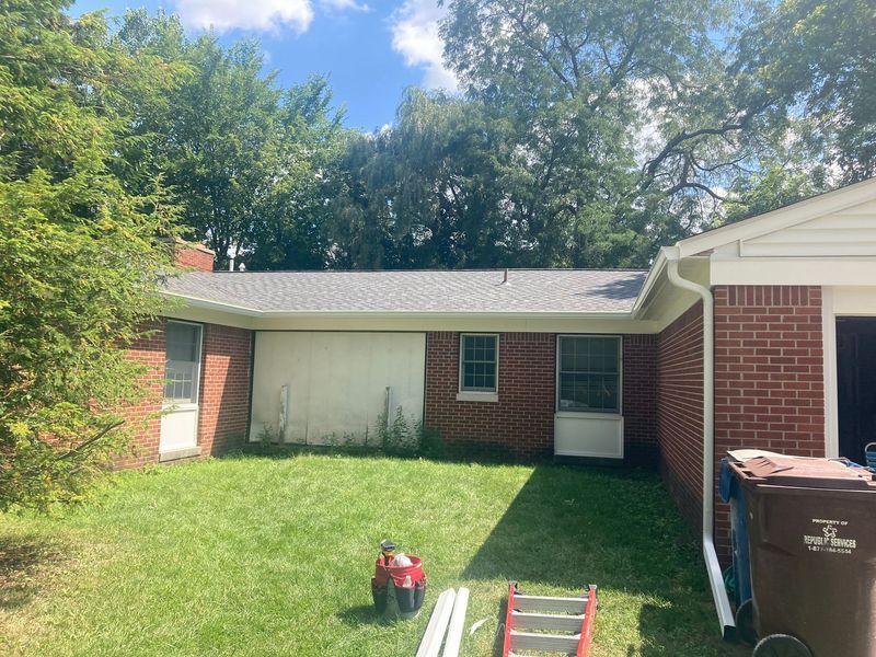 Brick house with new gray roof, green lawn, trees, and construction equipment.
