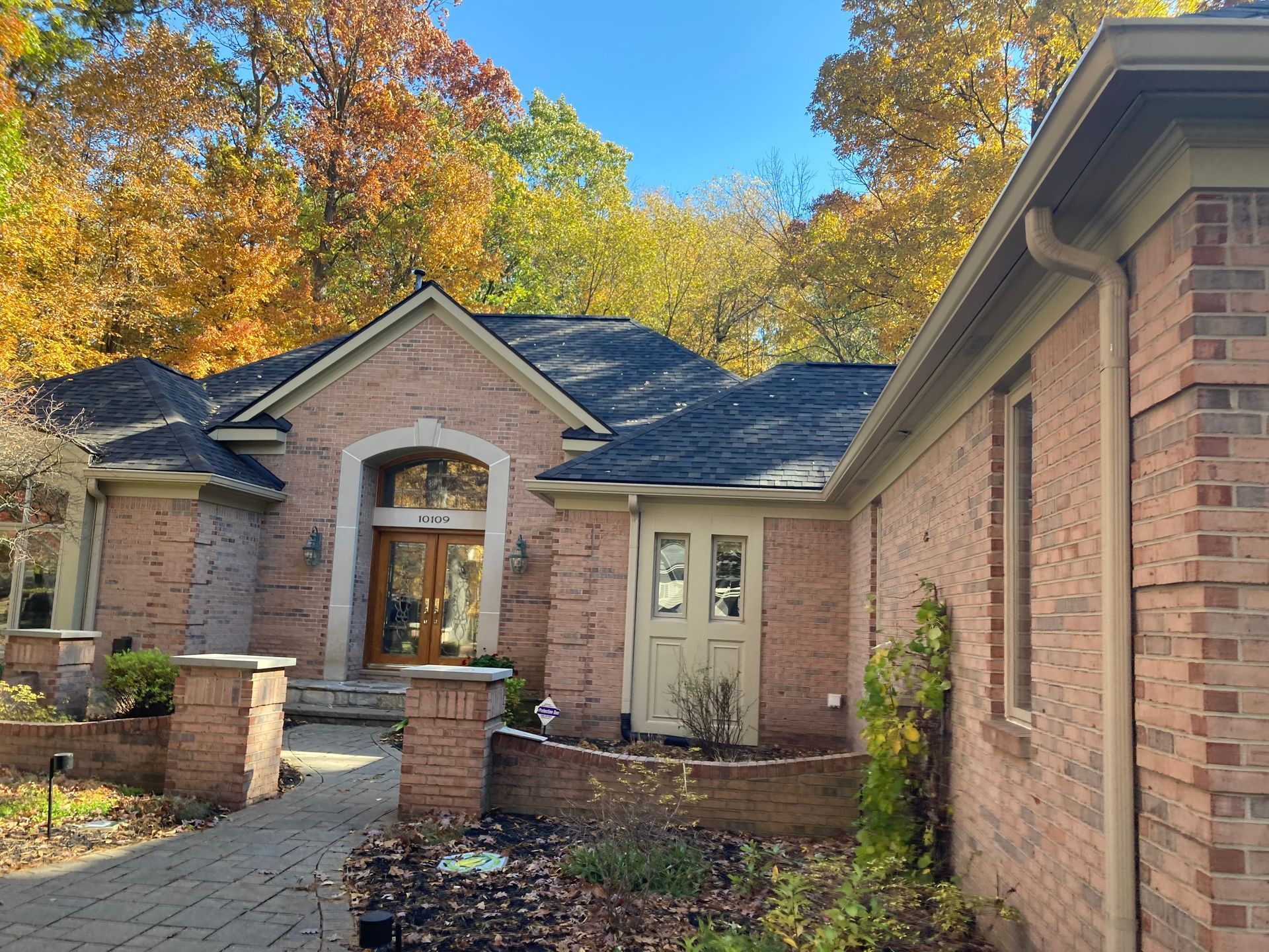 Brick home exterior with a dark roof and autumn trees.