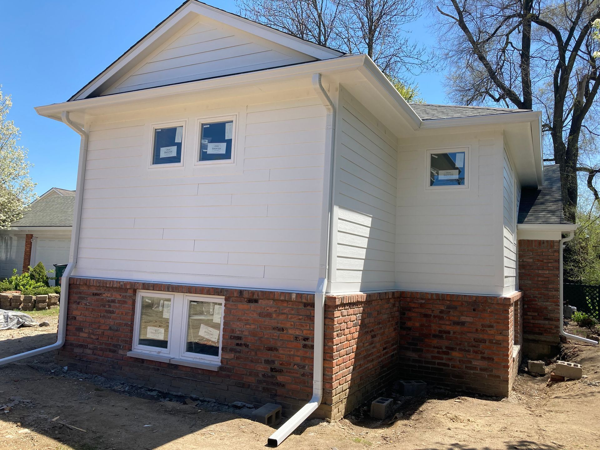 Exterior of a house under construction; white siding over brick, with two windows covered in blue wrap.