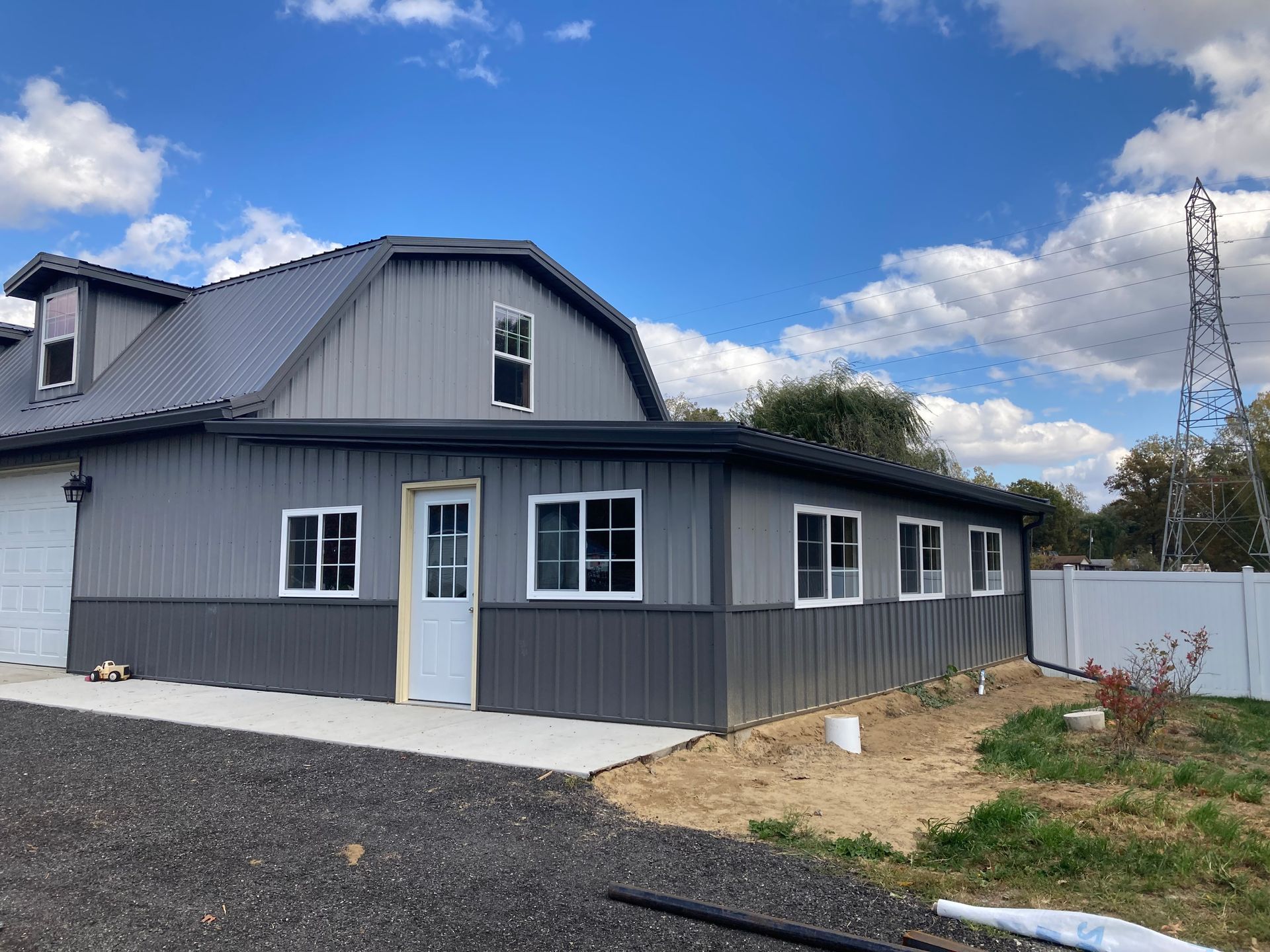 Gray barn with white-framed windows, a concrete walkway, and a clear blue sky.