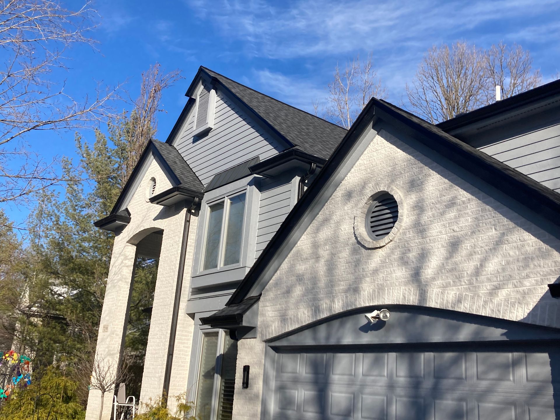 Two-story house with gray siding, black trim, and a gray garage door against a blue sky.