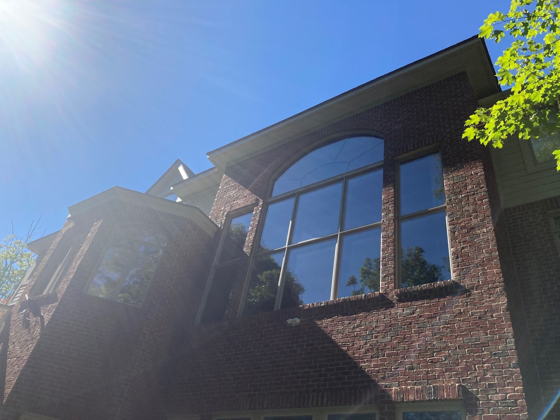 Brick house with large arched window reflecting sky and trees on a sunny day.