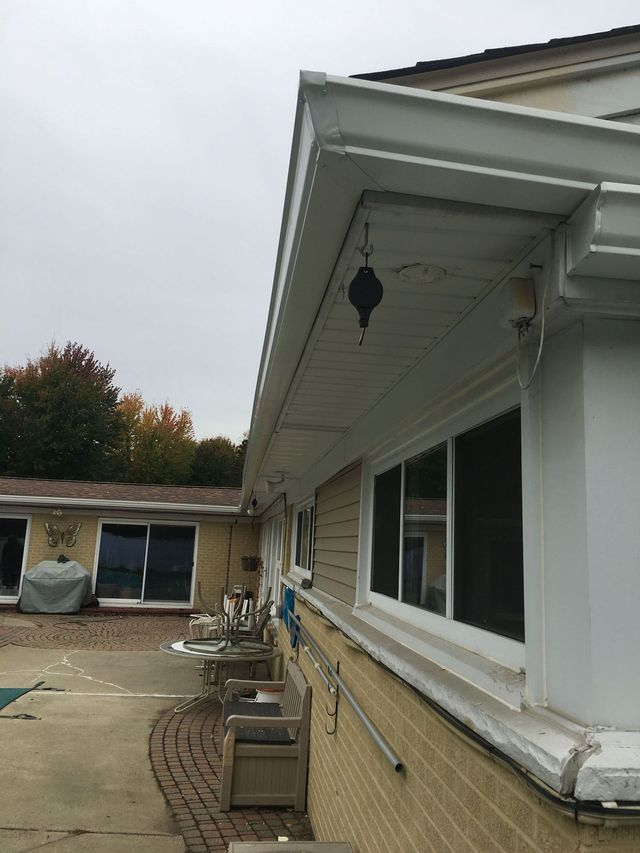 Exterior of a house with white gutters, beige siding, and windows. A decorative hanging object is visible.