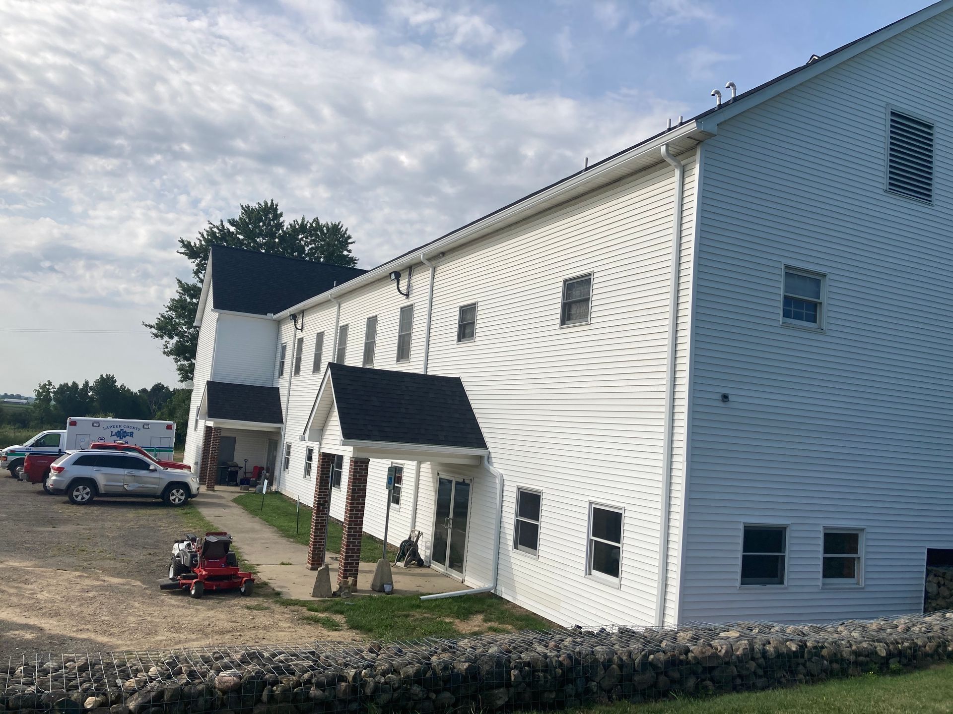 White two-story building with a black roof and several windows. Cars parked nearby.