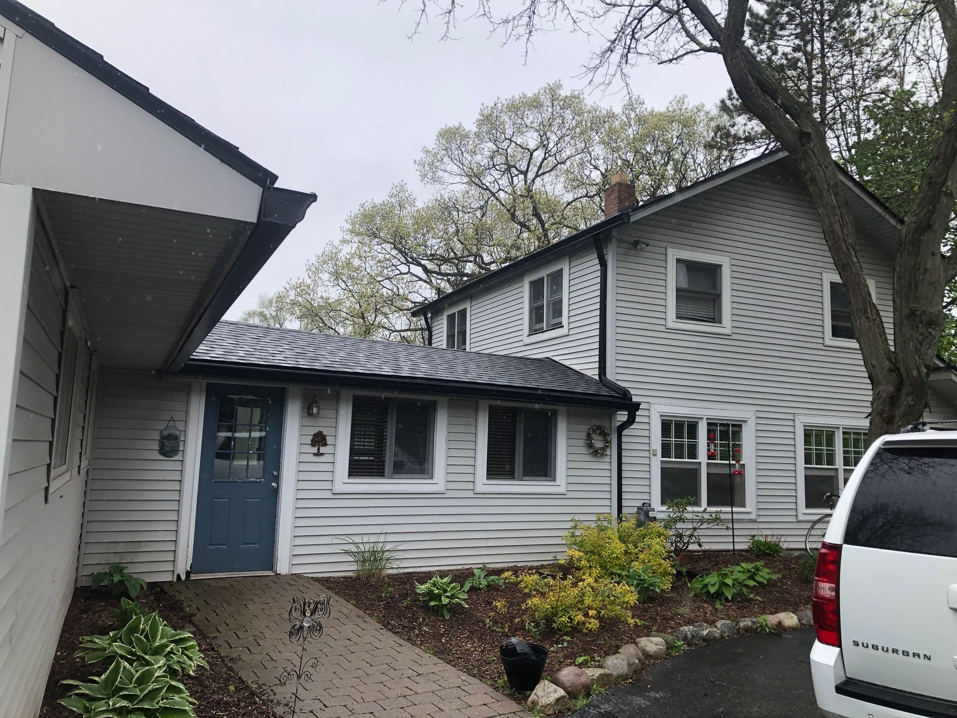 White two-story house with a blue door and a small connecting building, with a paved walkway.