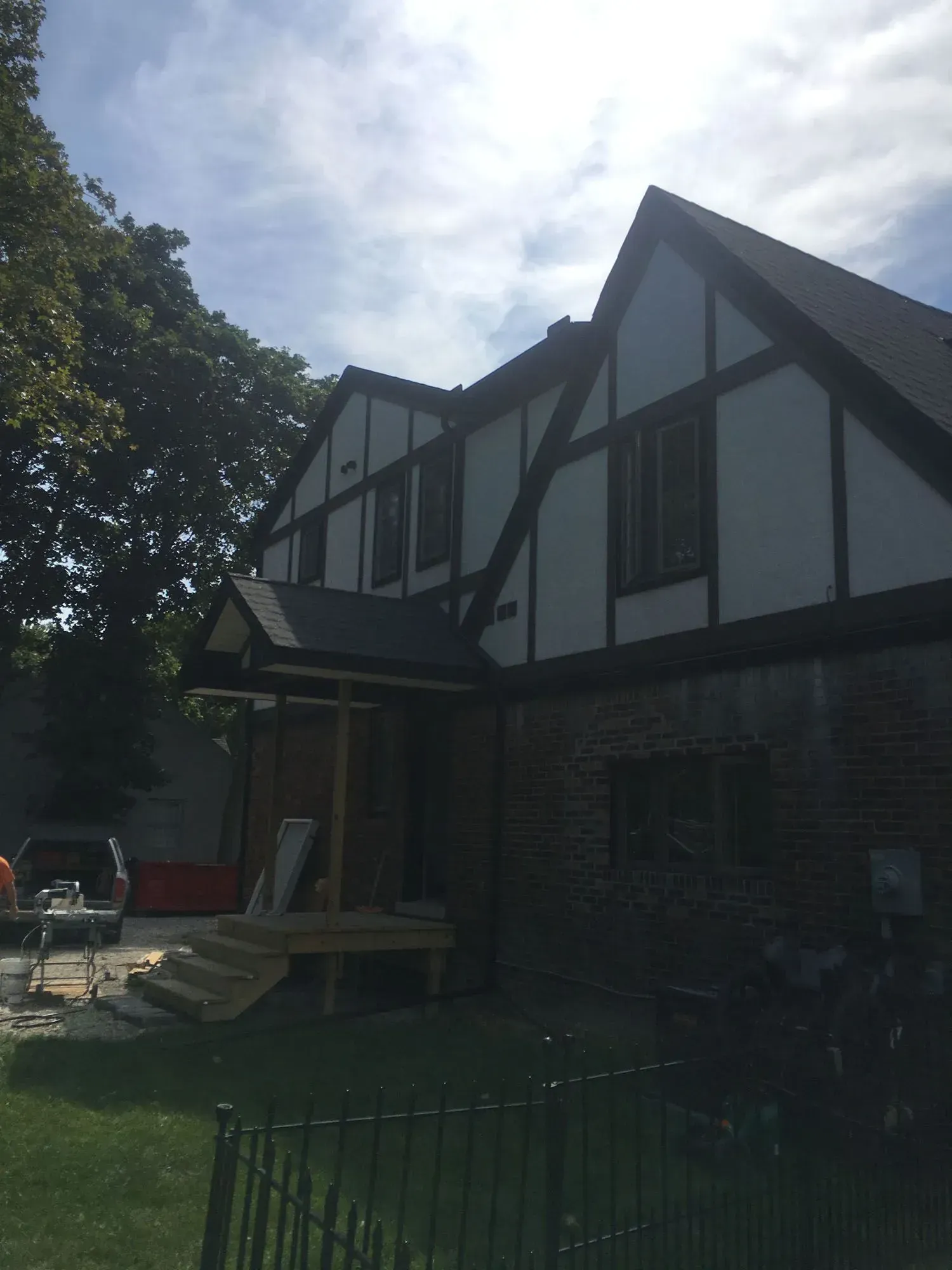 Two-story Tudor style house under construction with white stucco, dark trim, and a small porch.