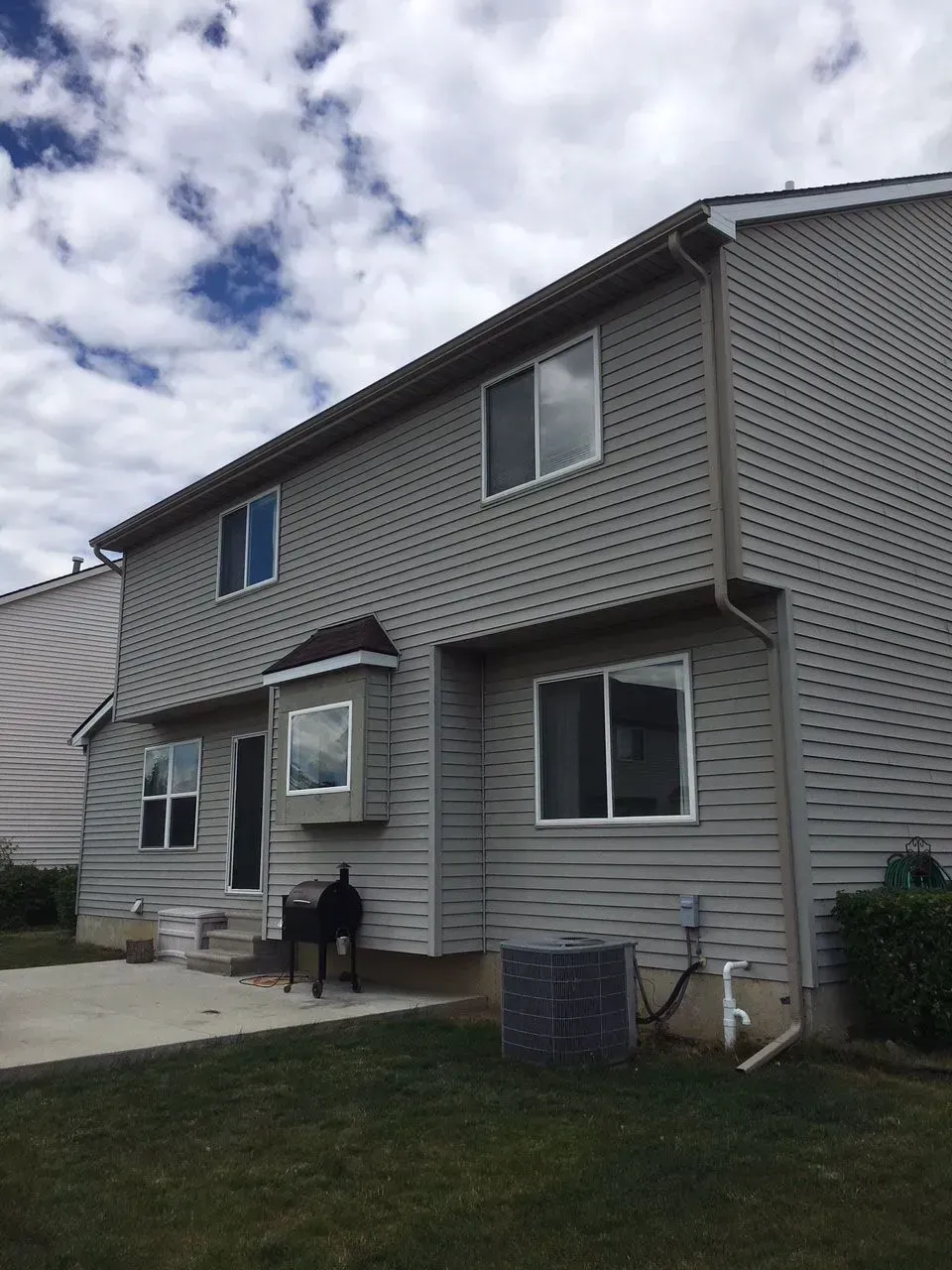 Two-story house with gray siding, windows, and a bay window, under a cloudy sky.