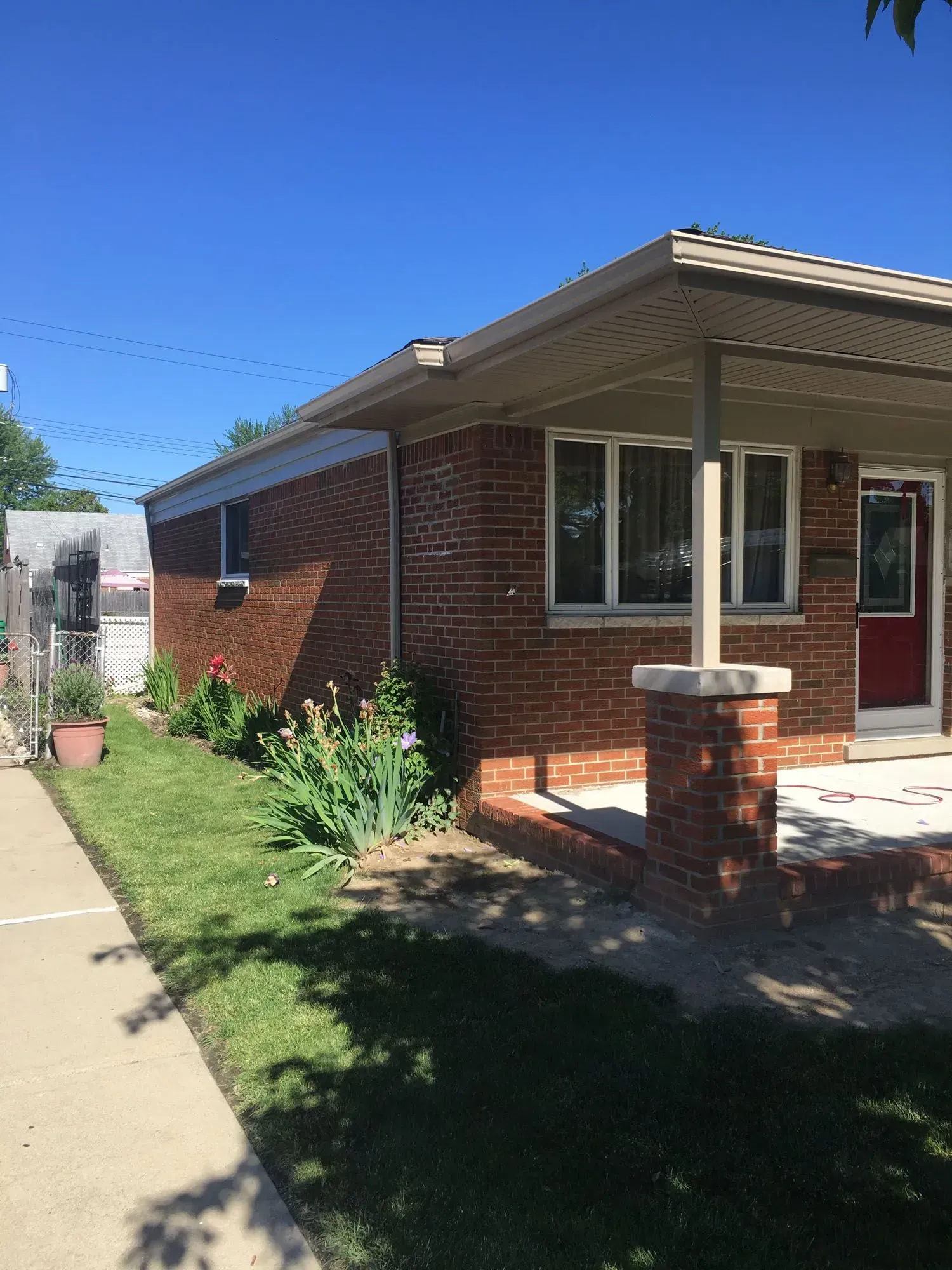 Brick house with a small porch, green lawn, blue sky.