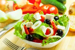 A salad with lettuce , tomatoes , olives and feta cheese in a bowl with a fork.