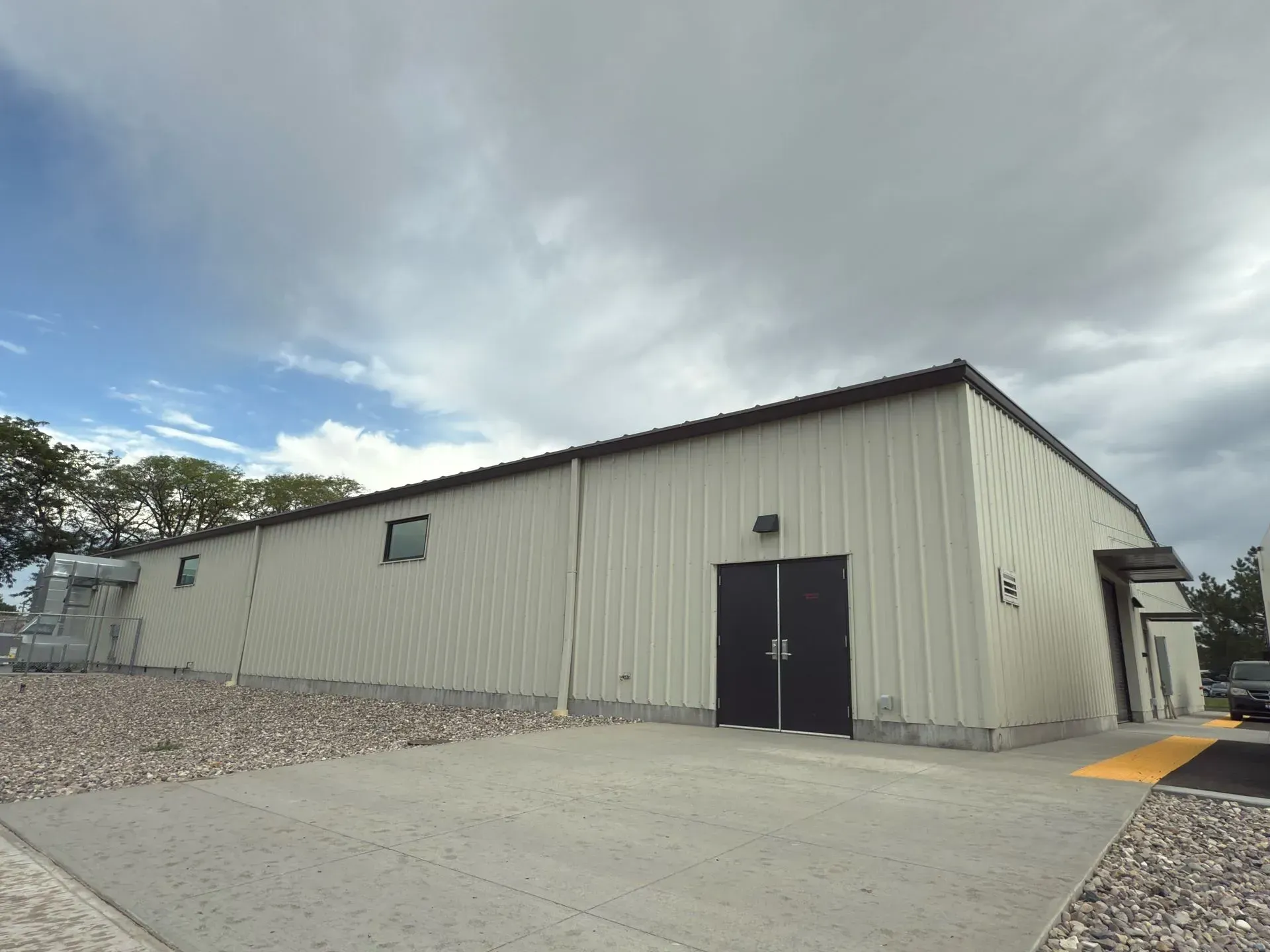 A light-colored metal building with a dark double door, set against a cloudy sky.