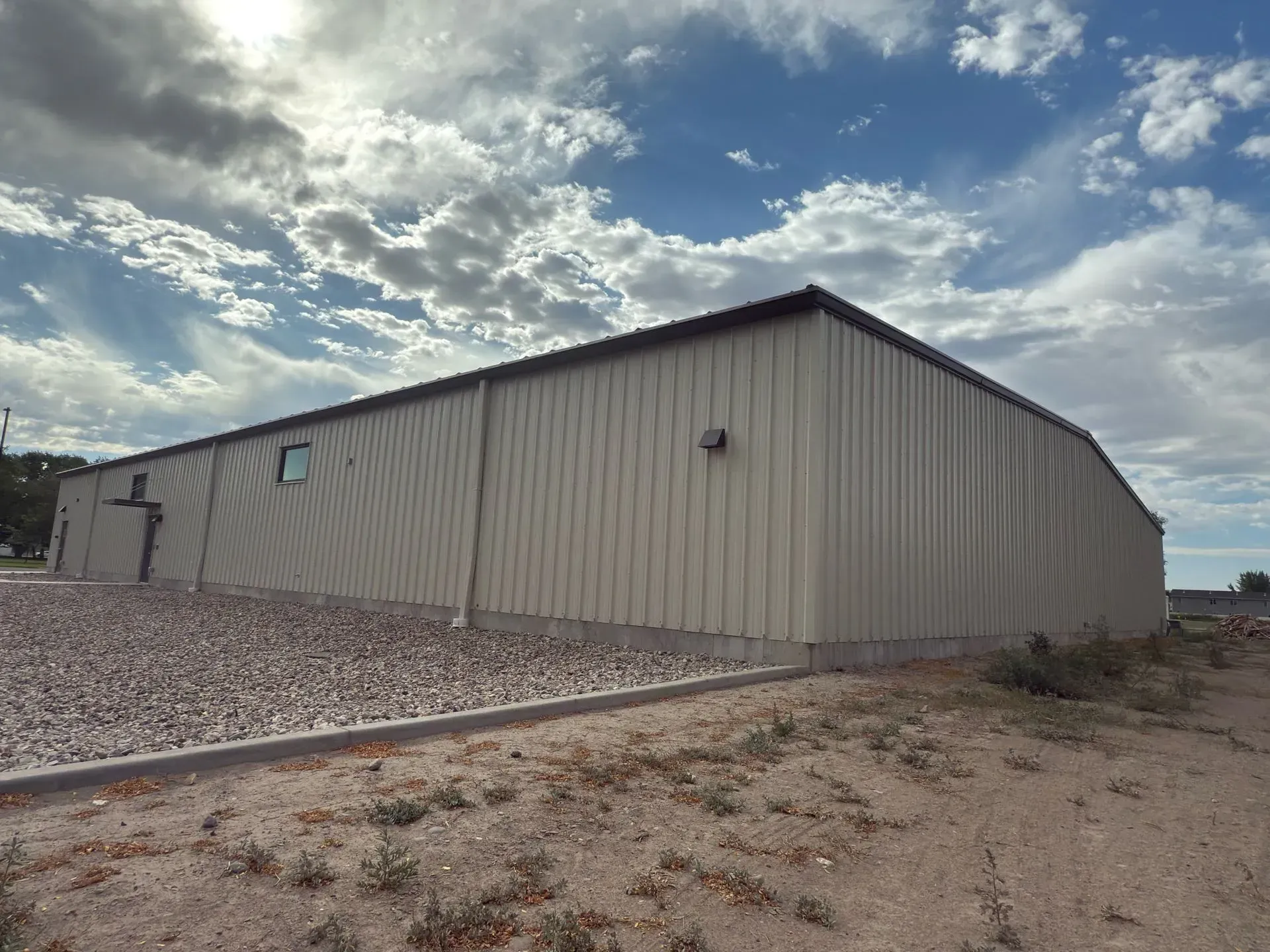 Metal building with beige siding and a brown roof against a cloudy blue sky.