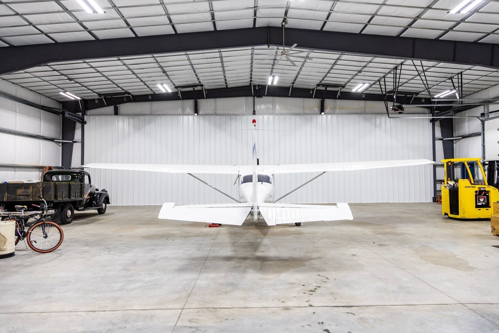A small plane is parked in a hangar next to a truck and a bicycle.