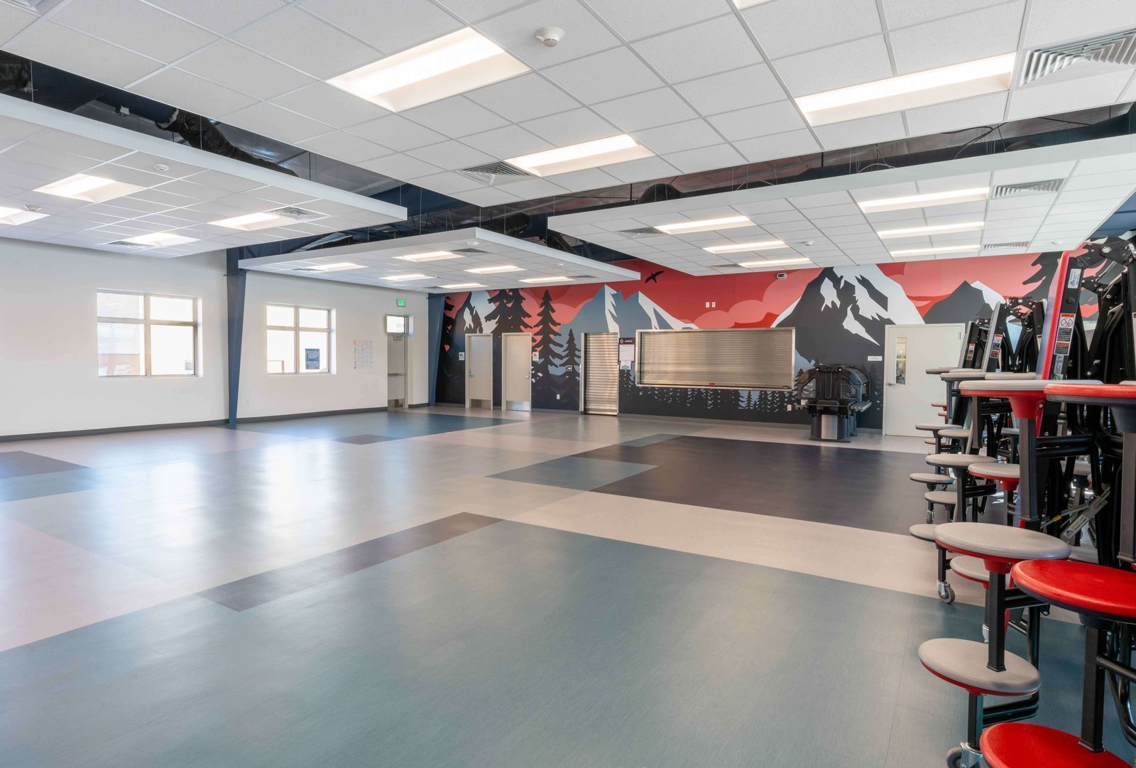 A large empty room with tables and chairs and a mural on the wall.