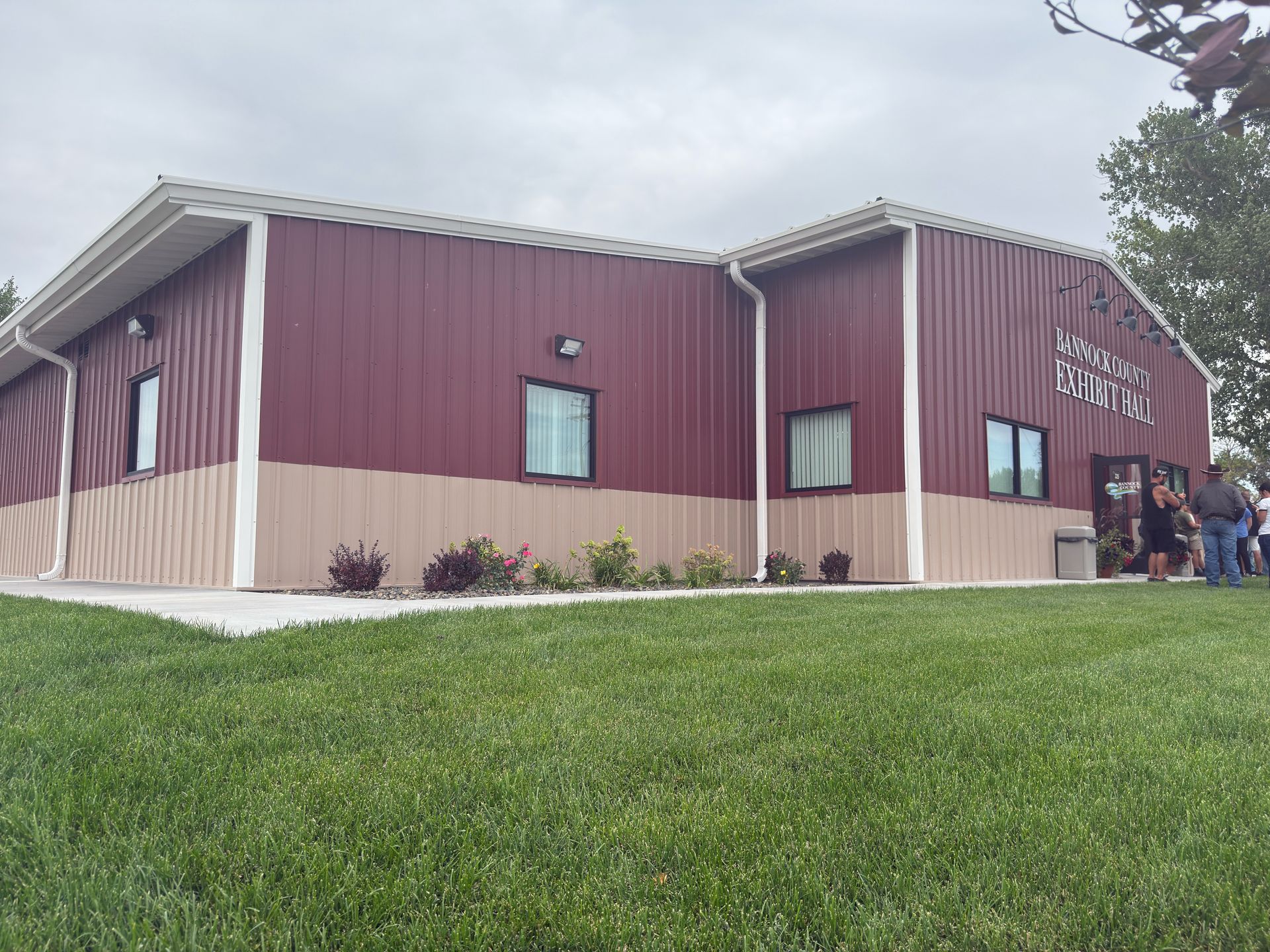 Red and tan metal building with small windows, a concrete walkway, and a grassy lawn.