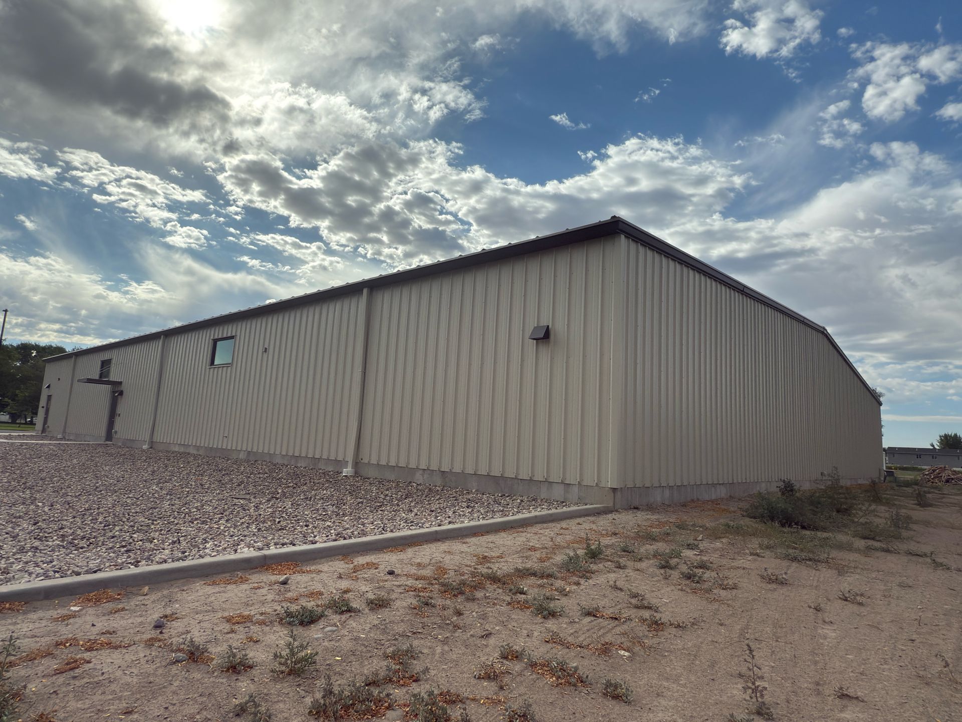 Metal building with beige siding and a brown roof against a cloudy blue sky.