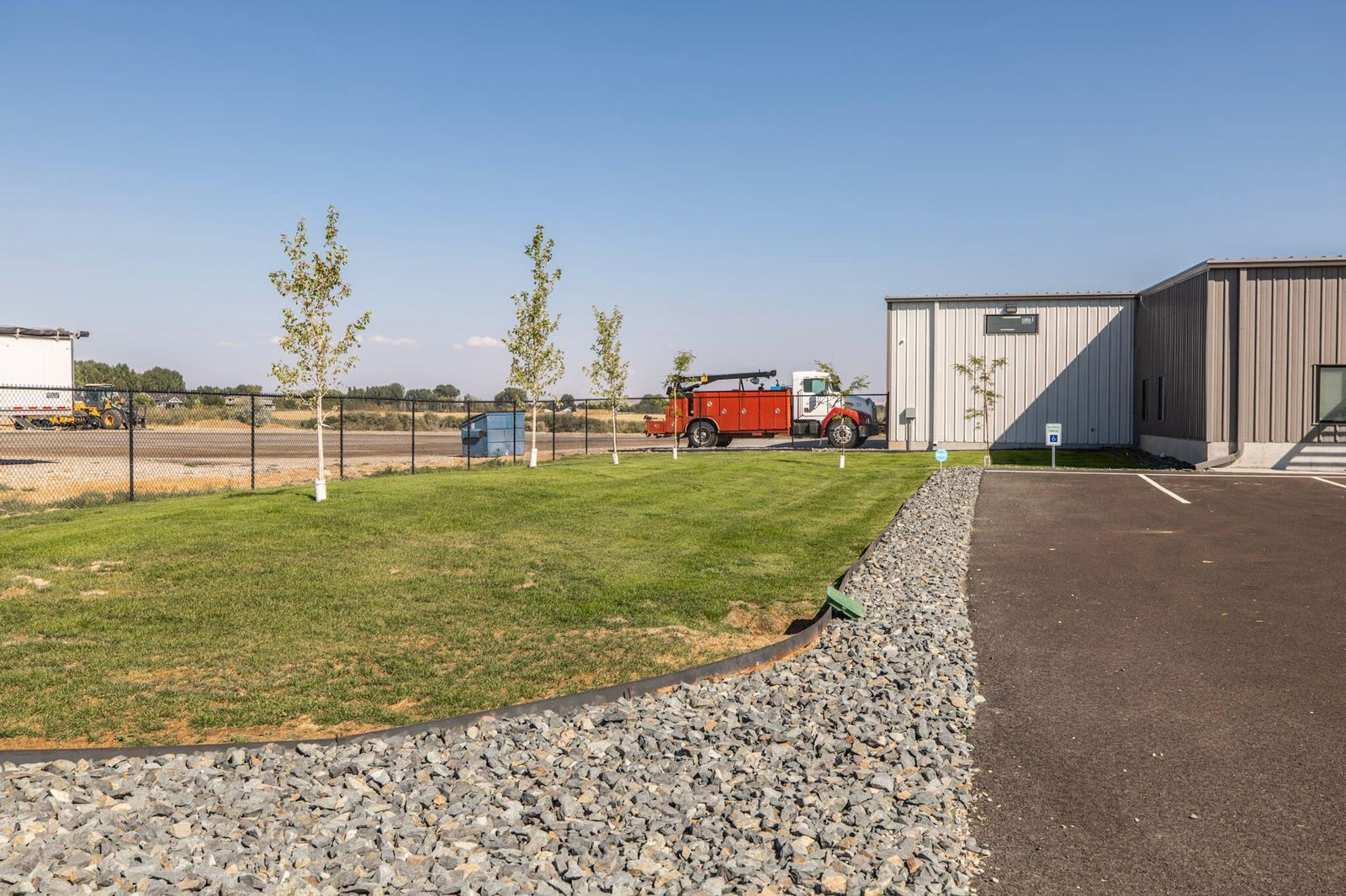 Grassy area with gravel border, trees, and truck next to a building