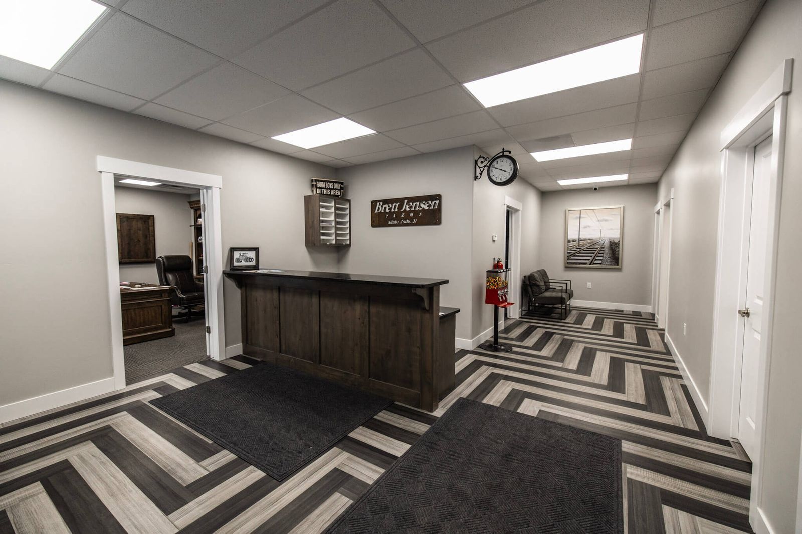 Reception area with wood-look flooring, dark wooden reception desk, and a view into an office