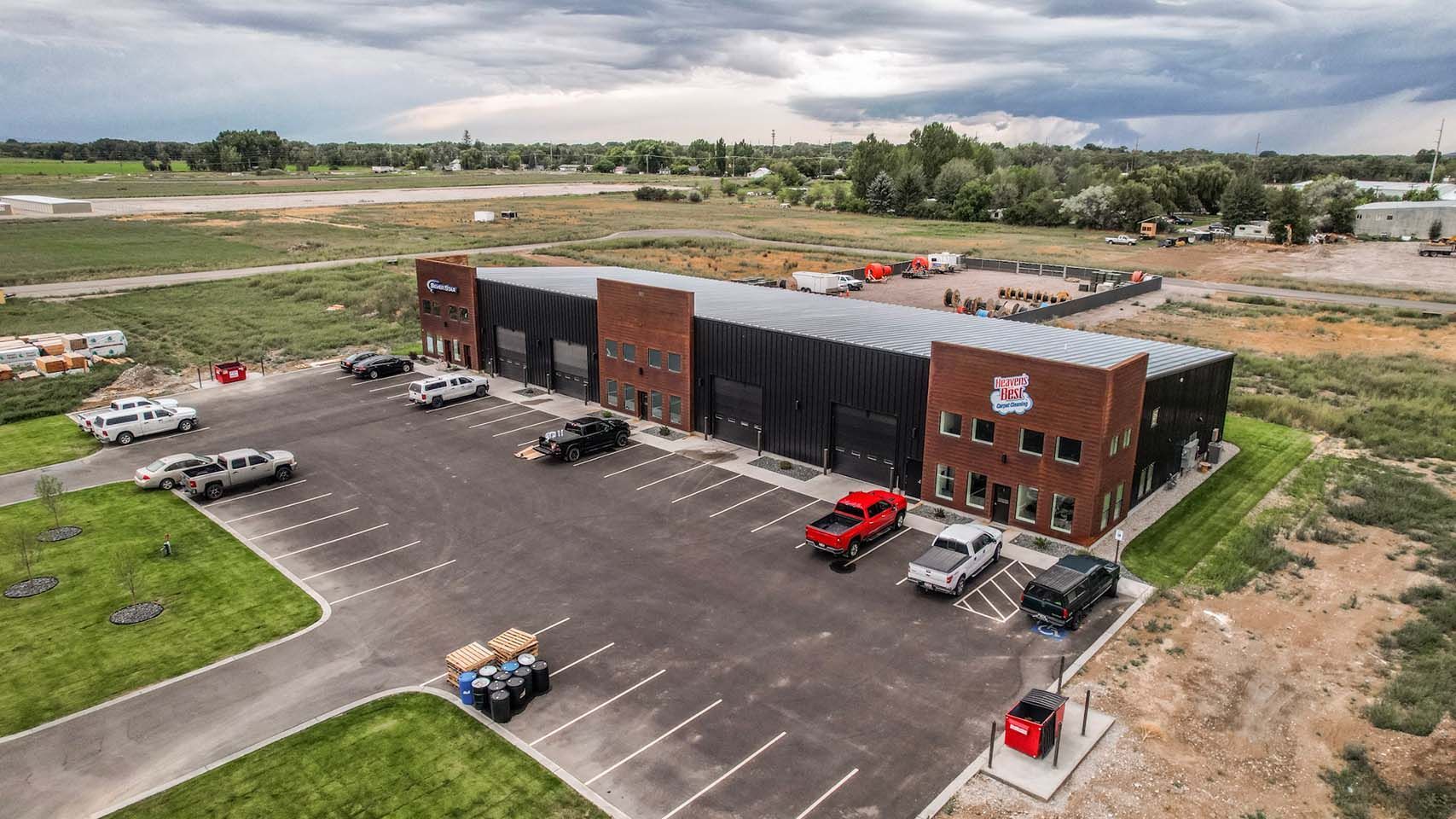A long, dark building with red brick accents, a large parking lot, and various vehicles