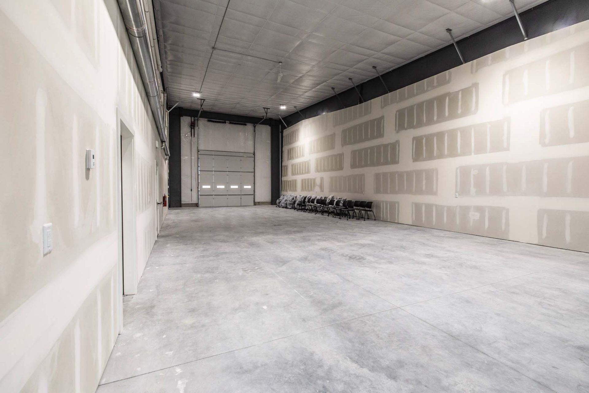 Empty warehouse interior with unfinished drywall, concrete floor, and a large overhead door