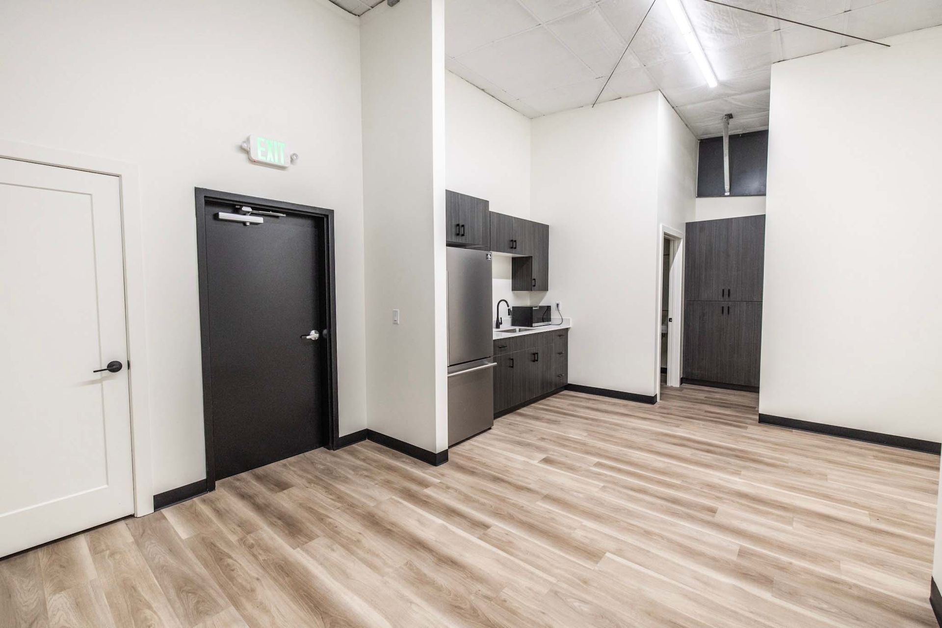 Empty office break room with kitchen appliances, dark cabinets, and wood-look floors