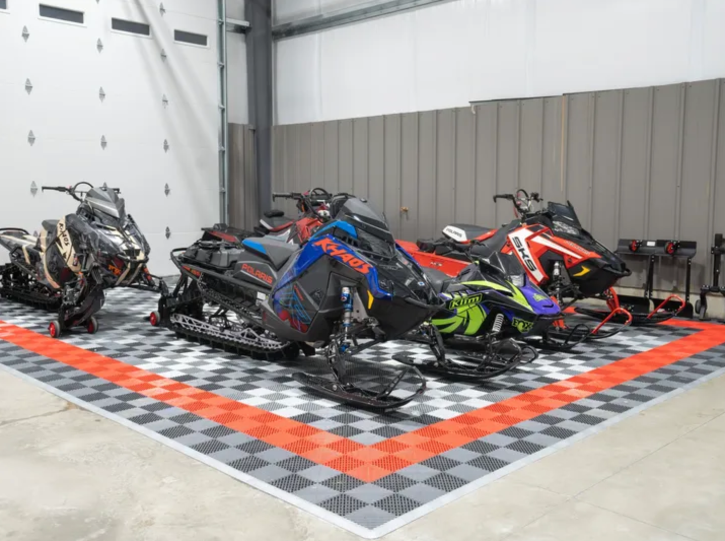 A row of snowmobiles are parked in a garage.