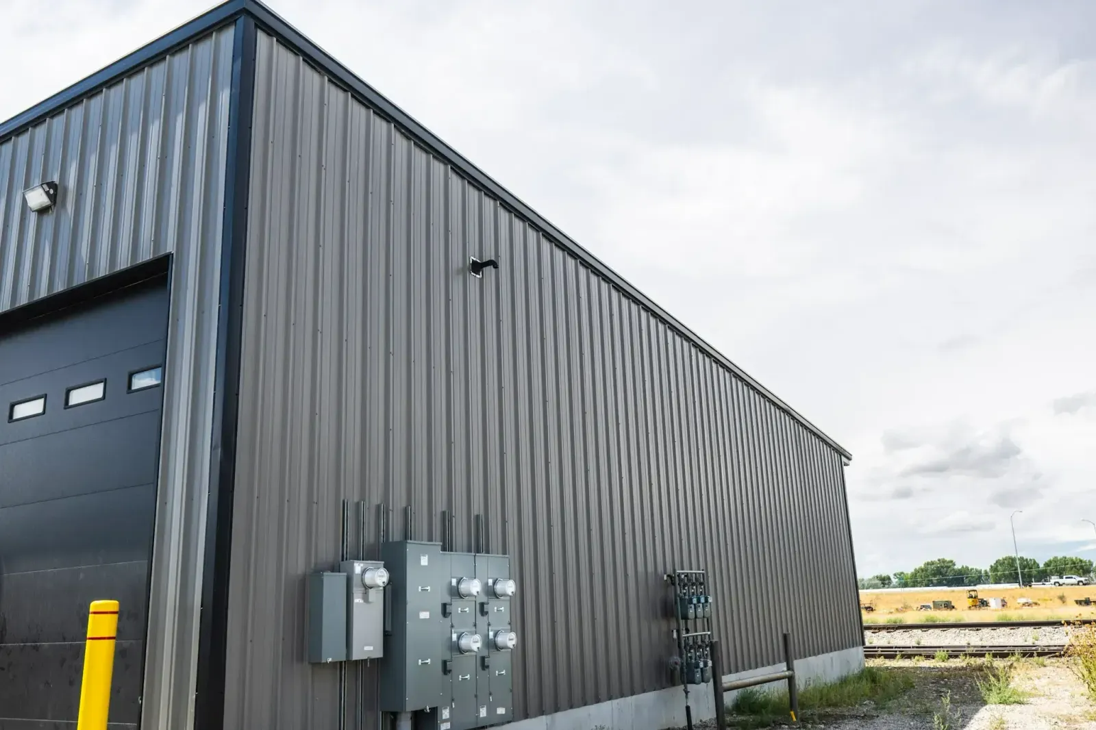 A large metal building with a garage door and electrical boxes on the side.