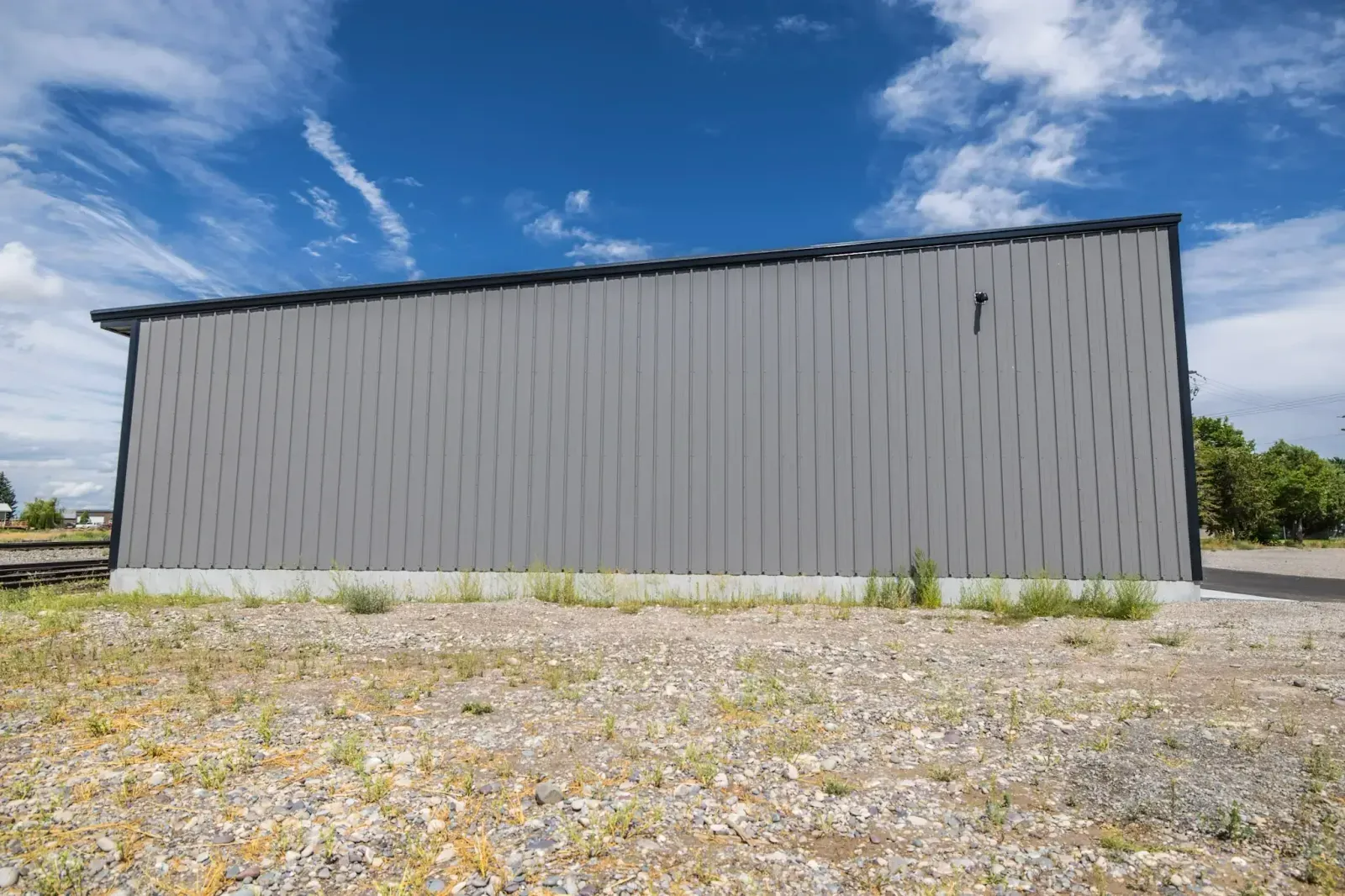 A large gray metal building is sitting on top of a gravel lot.
