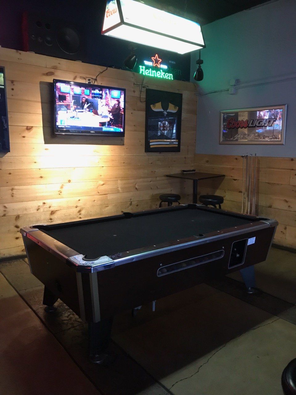 A pool table in a bar with a television on the wall.