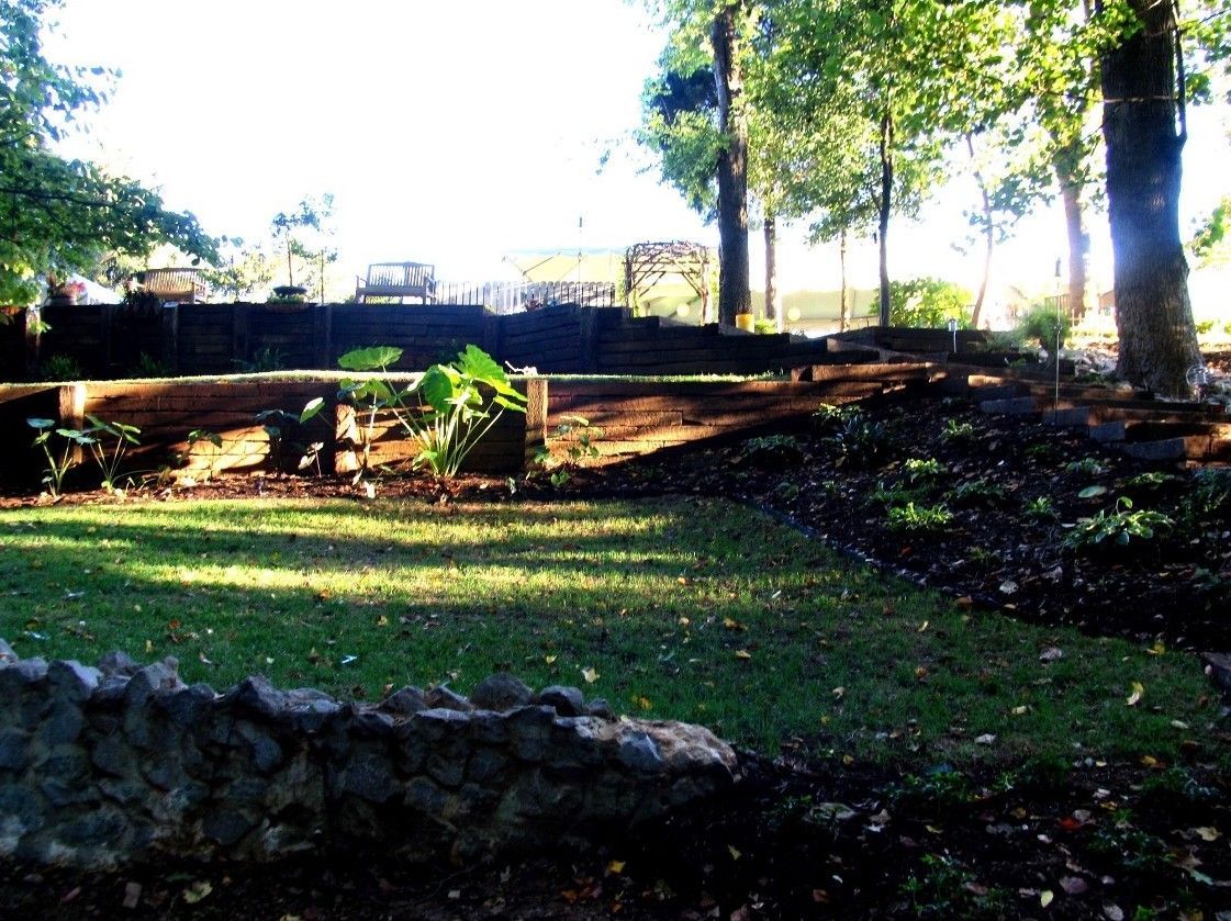 Sunlit park with stone walls, grass, trees, and tiered landscaping.