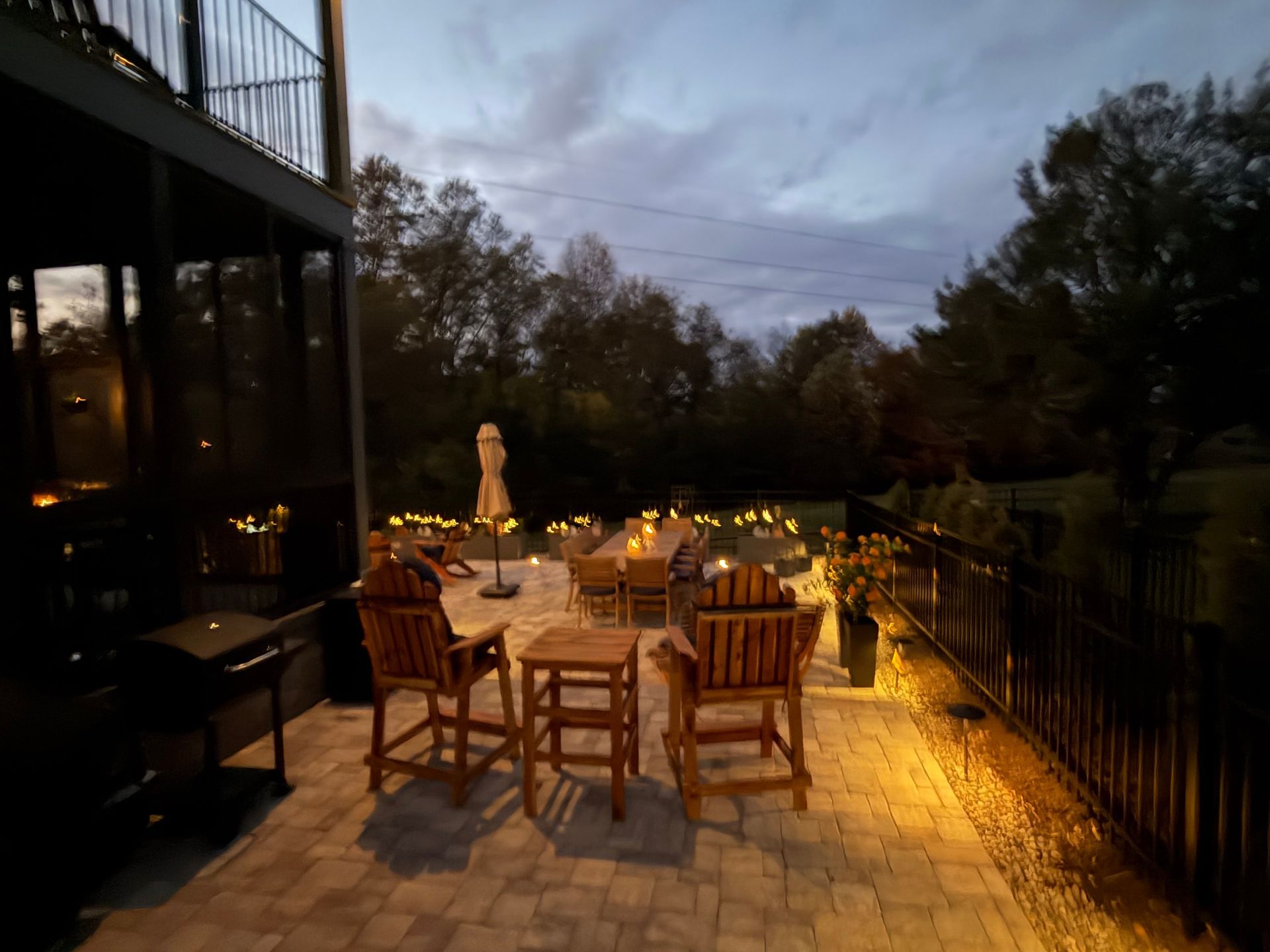 Patio at dusk with wooden furniture, string lights, and a dark cloudy sky.