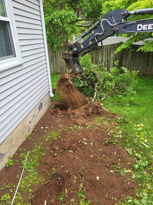 Excavator digging a trench beside a house, with soil piled along the foundation.