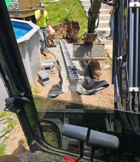 Excavator view of workers installing a drainage trench beside an above-ground pool in a backyard