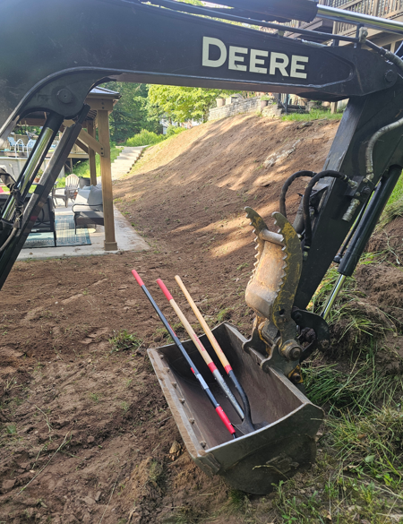 John Deere excavator bucket with construction flags on a dirt slope