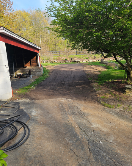 Farm driveway beside a red-roofed barn, with a tree and dirt path in the foreground.
