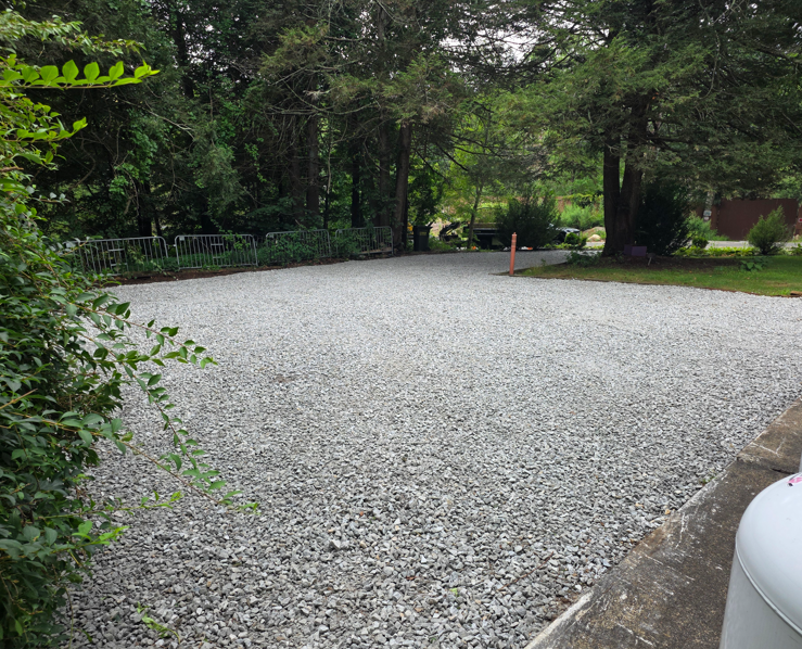 Gravel driveway bordered by trees and shrubs, with a small orange marker near the center.