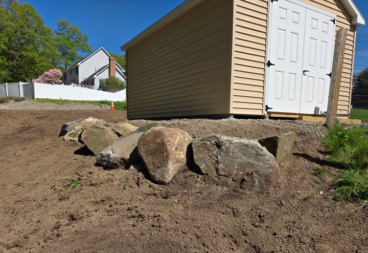 Backyard shed beside a row of large rocks and freshly graded dirt