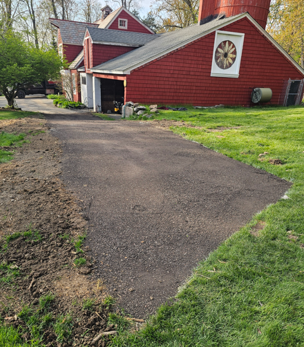 Cracked asphalt driveway beside a red house with white trim and a decorative round window