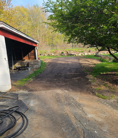 Gravel driveway beside a red outbuilding, with trees and a grassy yard in the background