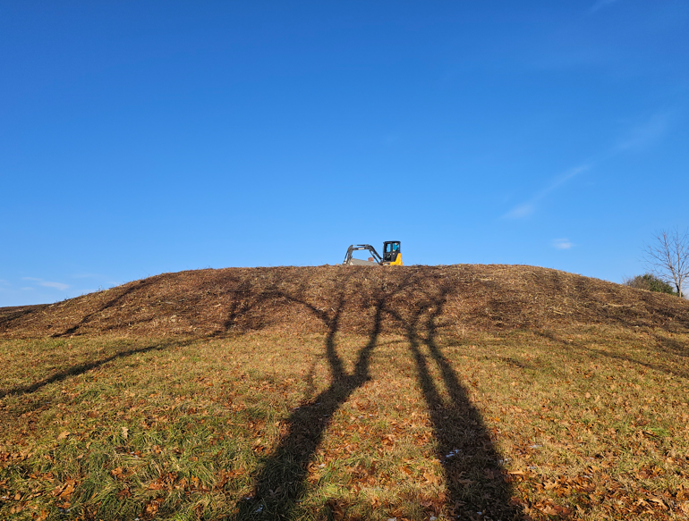 Small tractor on a grassy hill under a blue sky, with long shadows in the foreground.