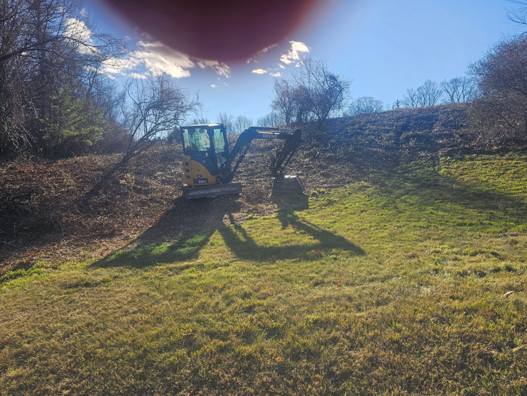 Small tractor on a grassy hillside under bright sun, with a person standing nearby.