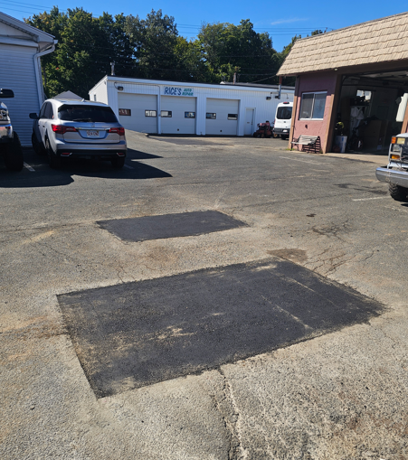 Parking lot with patchy asphalt, parked cars, and a white garage building in the background.
