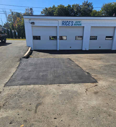 Auto body shop with a freshly patched asphalt area in front of garage doors on a sunny day