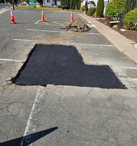 Fresh black asphalt patch on a cracked road with orange cones nearby in a parking lot